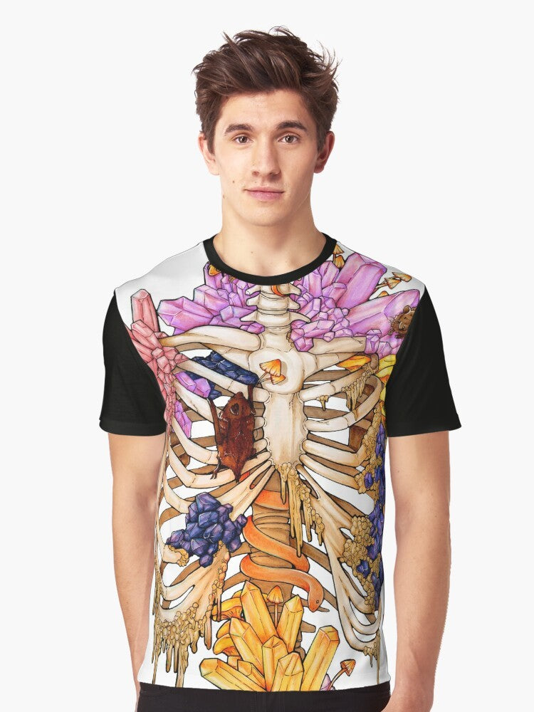 A graphic t-shirt featuring a hidden gem skeleton design in pink and purple colors, surrounded by elements like bats, snakes, mushrooms, and rocks. - Men