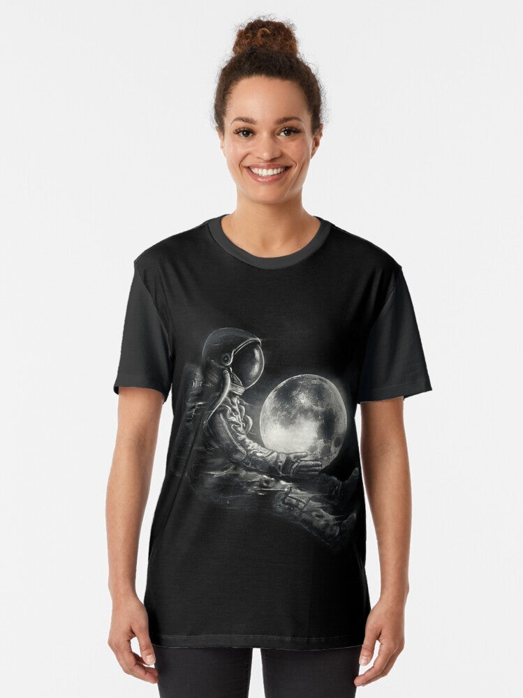 A black and white graphic t-shirt featuring a surreal, cosmic design with an astronaut or spaceman playing on the moon. - Women