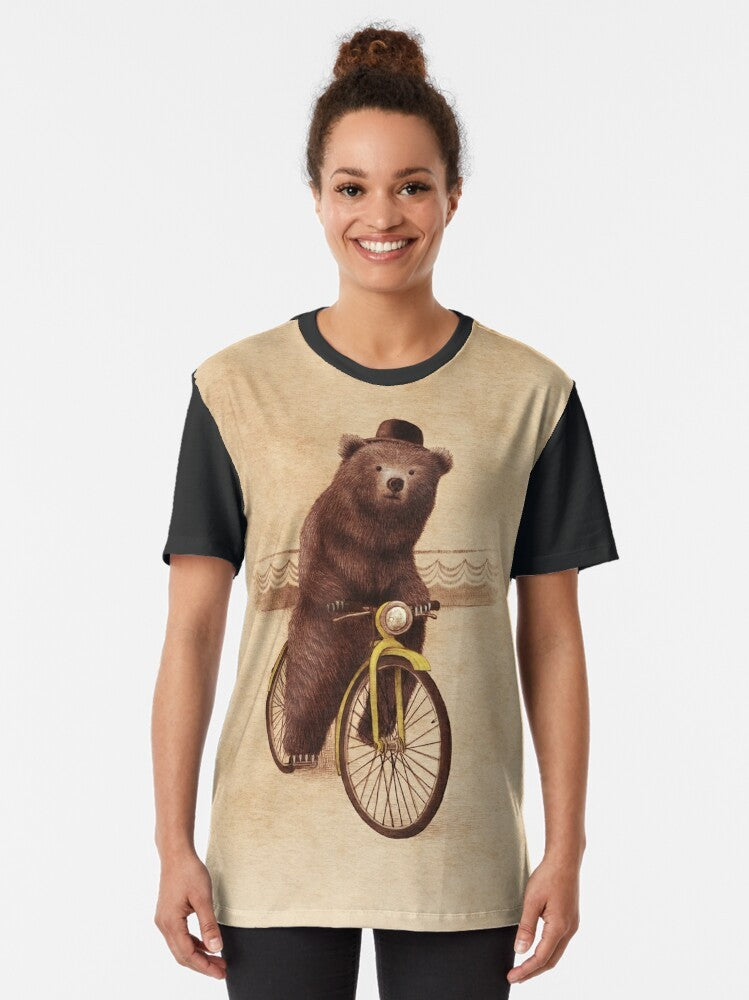 A whimsical graphic t-shirt featuring a vintage-style illustration of a bear riding a bicycle, wearing a bowler hat against a sepia-toned background. - Women