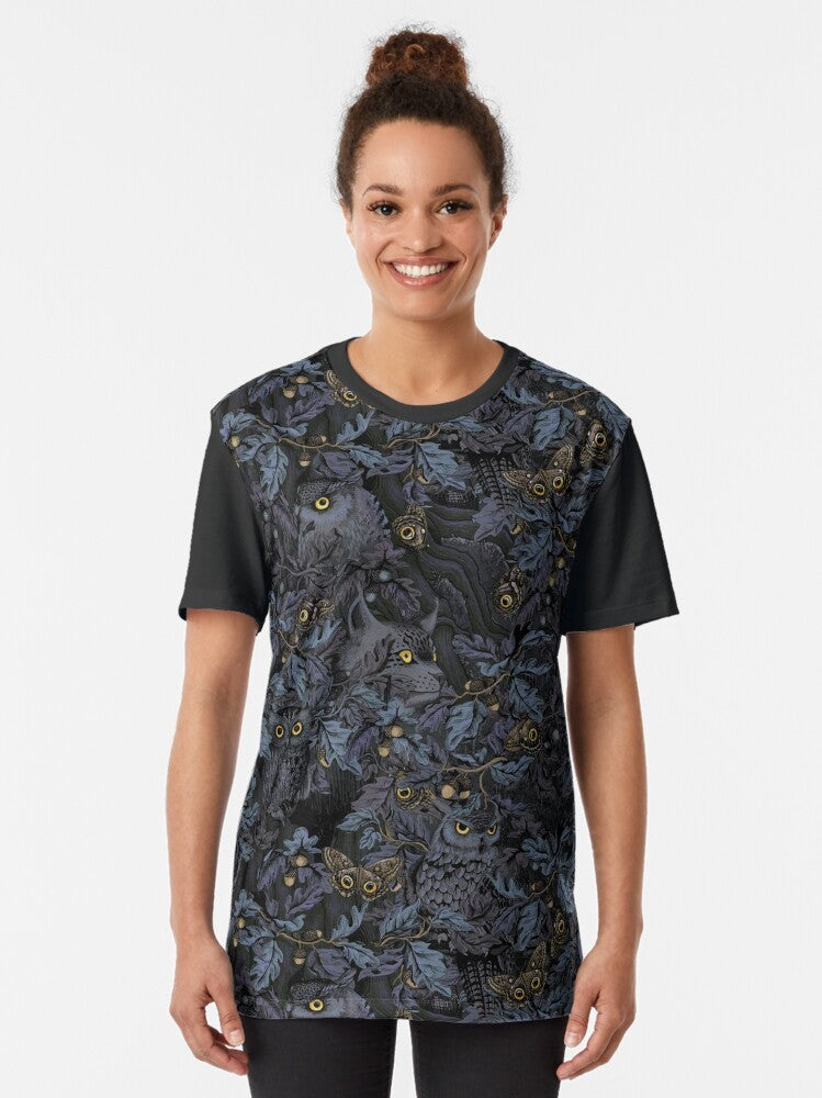 A graphic t-shirt featuring a camouflage pattern with owls, leaves, and moonlight imagery, capturing the beauty of nature's wilderness. - Women