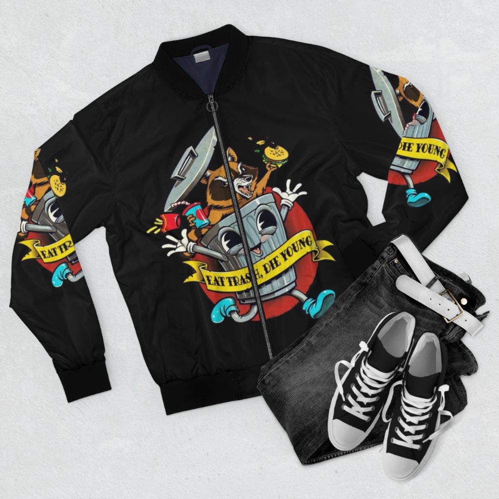 Vintage cartoon "Eat Trash Die Young" bomber jacket with raccoon, trash can, and other trash-themed graphics. - Flat lay