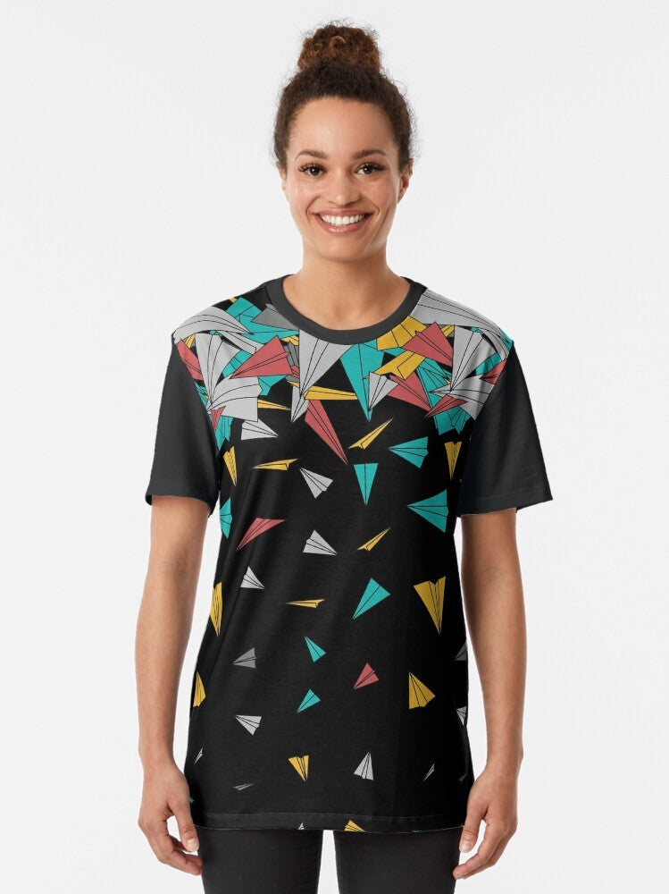 A colorful, abstract graphic t-shirt featuring a design of paper planes floating on a geometric pattern. - Women