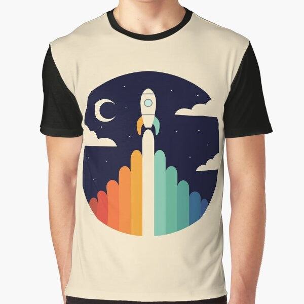 A graphic t-shirt featuring a rocket ship soaring through the sky, with a rainbow and clouds in the background, representing dreams and space exploration.