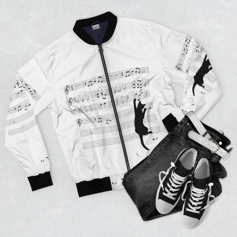 A black and white bomber jacket with a surreal design of a cat playing with sheet music and musical notes, showcasing a mischievous and playful nature. - Flat lay