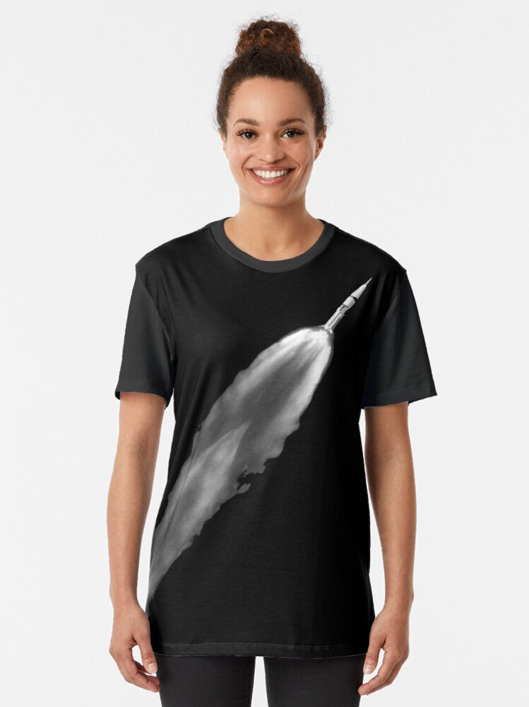 Graphic t-shirt with a rocket launch design, featuring the Saturn V rocket and space elements. - Women