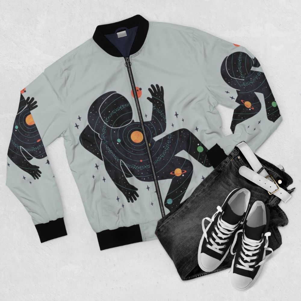 A minimalist bomber jacket featuring a space-inspired design with planets, stars, and cosmic elements. - Flat lay