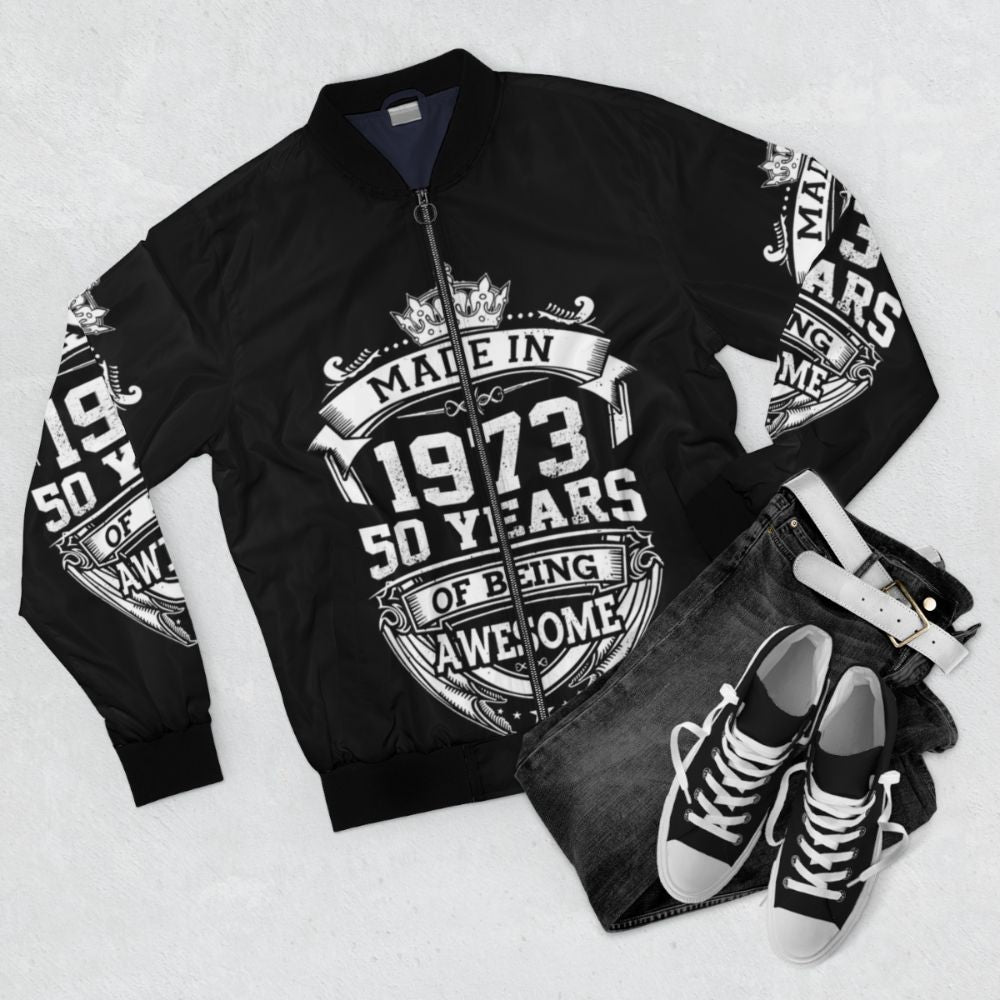 50th birthday bomber jacket made in 1973, featuring vintage 1973 design and "50 Years Of Being Awesome" text - Flat lay