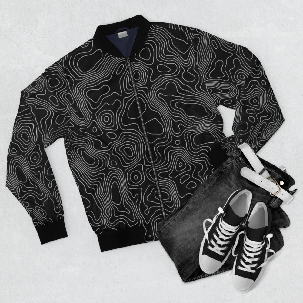 A minimalist bomber jacket featuring a topographic contour line abstract design in black and white. - Flat lay