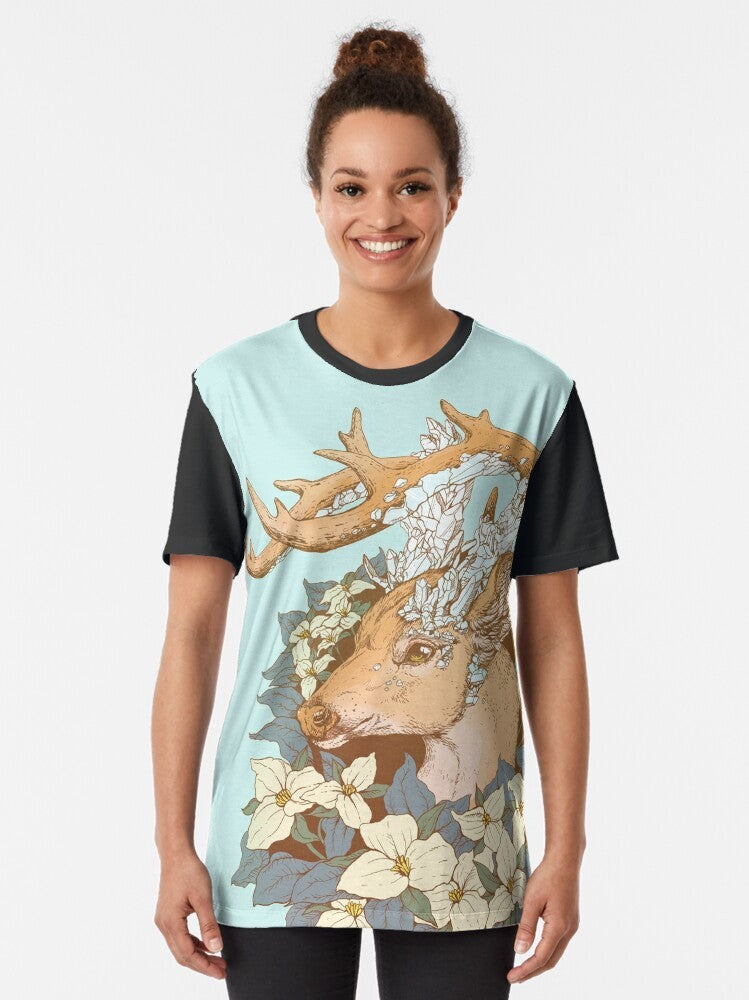 A graphic t-shirt featuring a non-typical blue quartz buck design with antlers and trillium flowers in a nature-inspired illustration. - Women