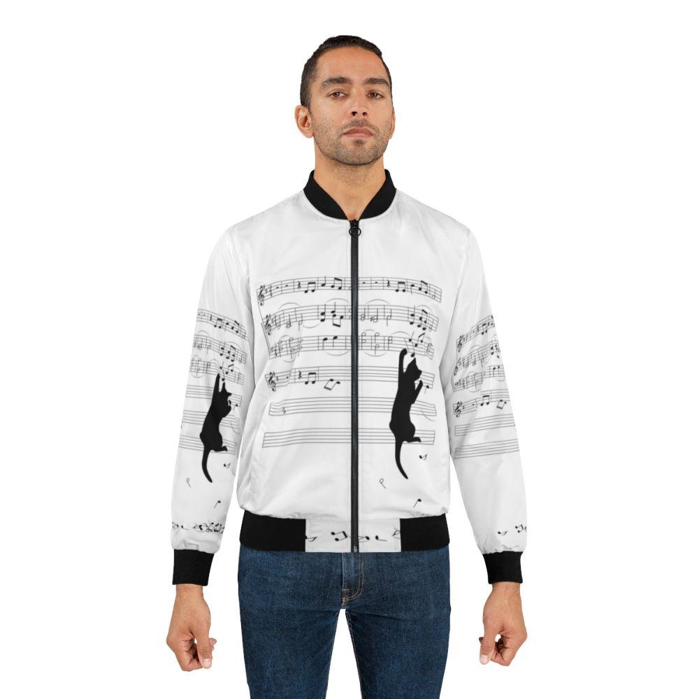 A black and white bomber jacket with a surreal design of a cat playing with sheet music and musical notes, showcasing a mischievous and playful nature. - Lifestyle