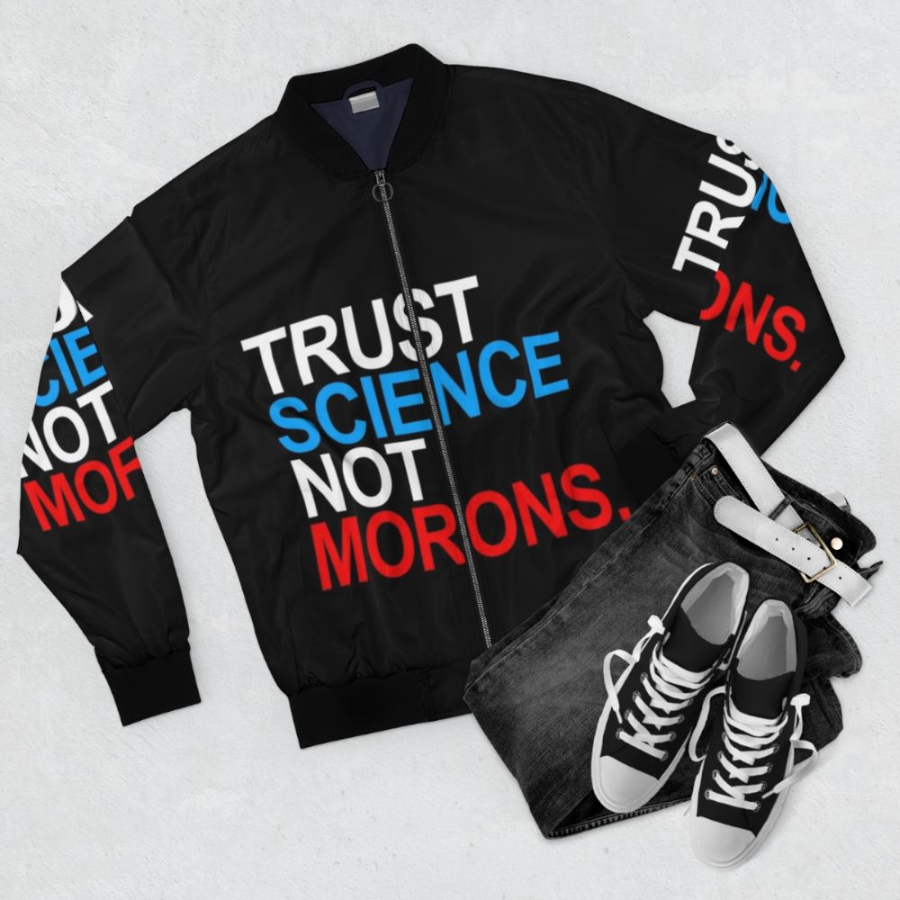 A red, white, and blue bomber jacket with the text "TRUST SCIENCE NOT MORONS" printed on it, representing a pro-science and anti-Trump sentiment during the COVID-19 pandemic. - Flat lay