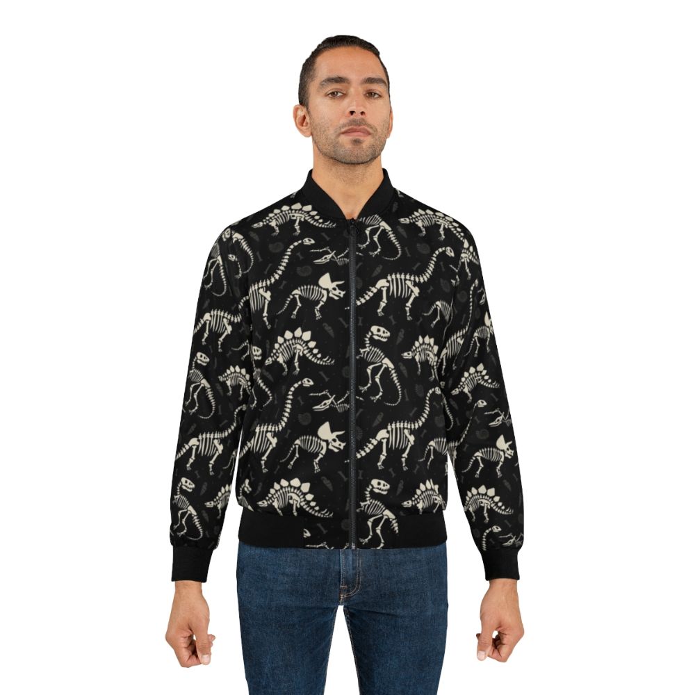 Black bomber jacket with a dinosaur fossil print design, featuring T-Rex, Triceratops, and other prehistoric creatures. - Lifestyle