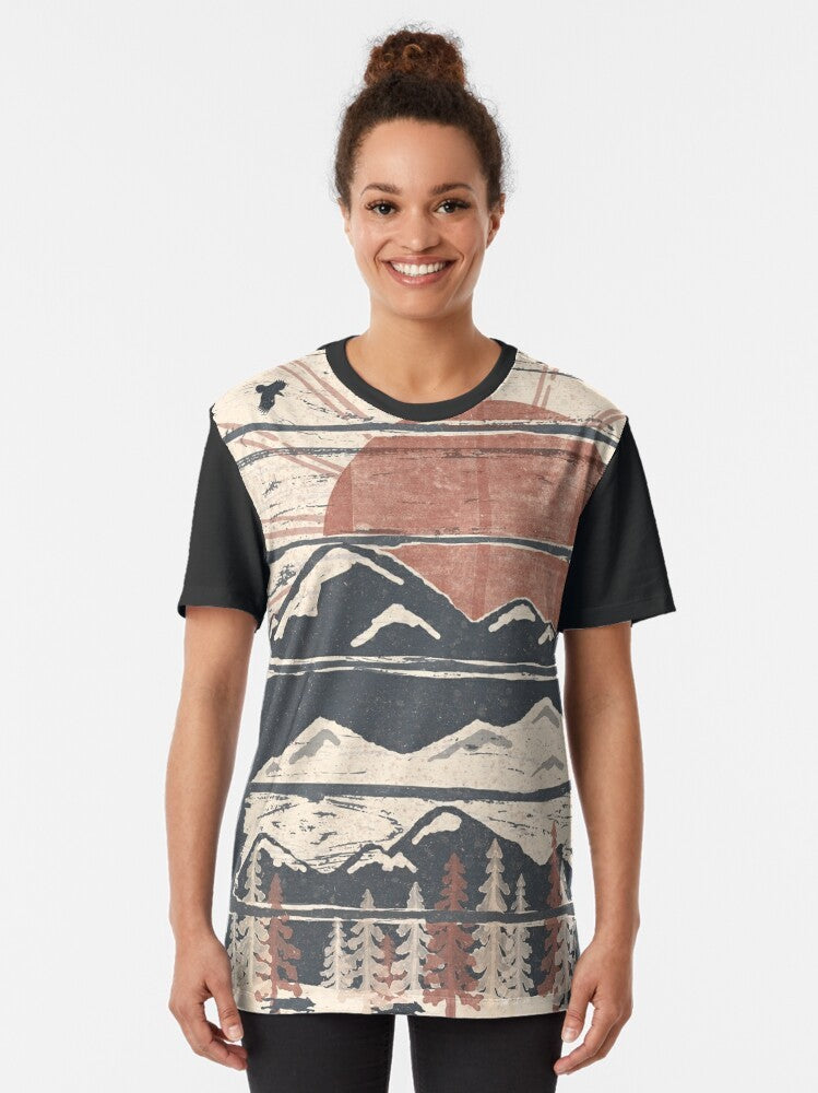 A graphic t-shirt featuring a winter landscape with wildlife such as wolves, hawks, and eagles. - Women