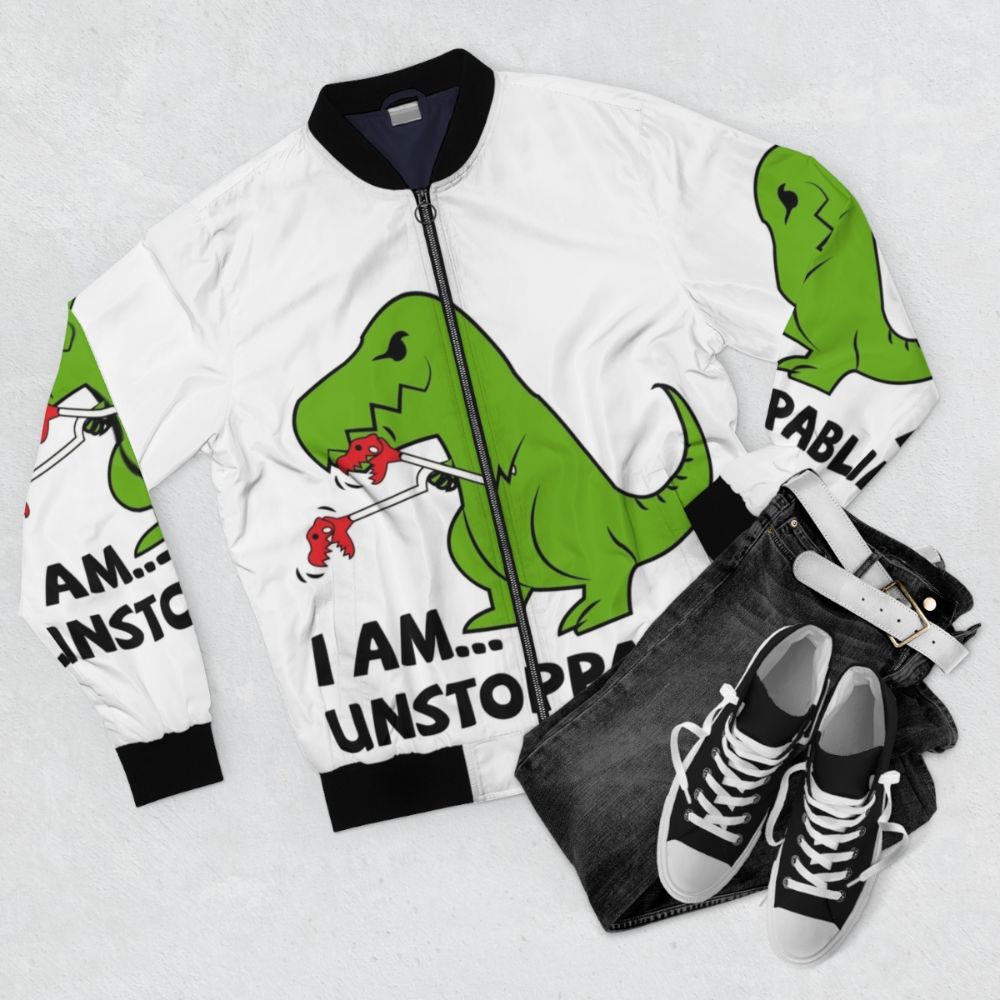 A green and red bomber jacket with a T-Rex print and the text "I am unstoppable" on it. - Flat lay