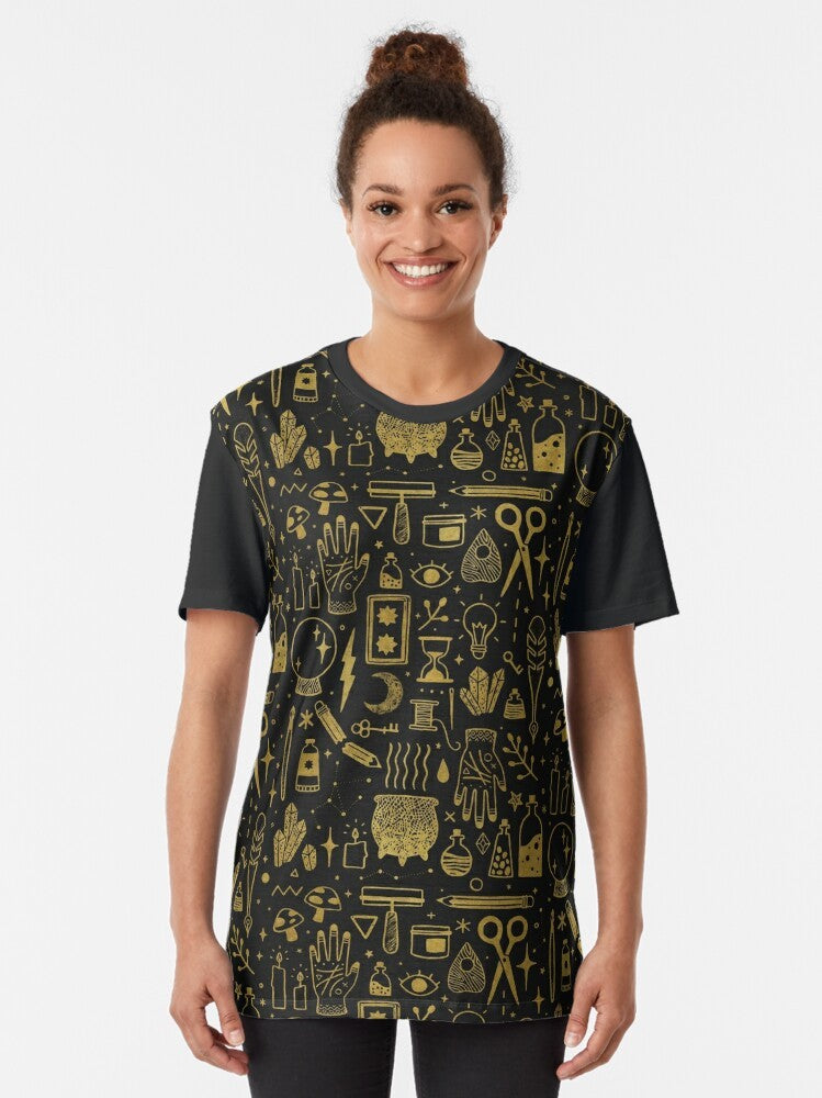 A gold and black graphic t-shirt featuring the words "Make Magic" with occult and witchy elements like a cauldron, mushrooms, and tarot cards. - Women