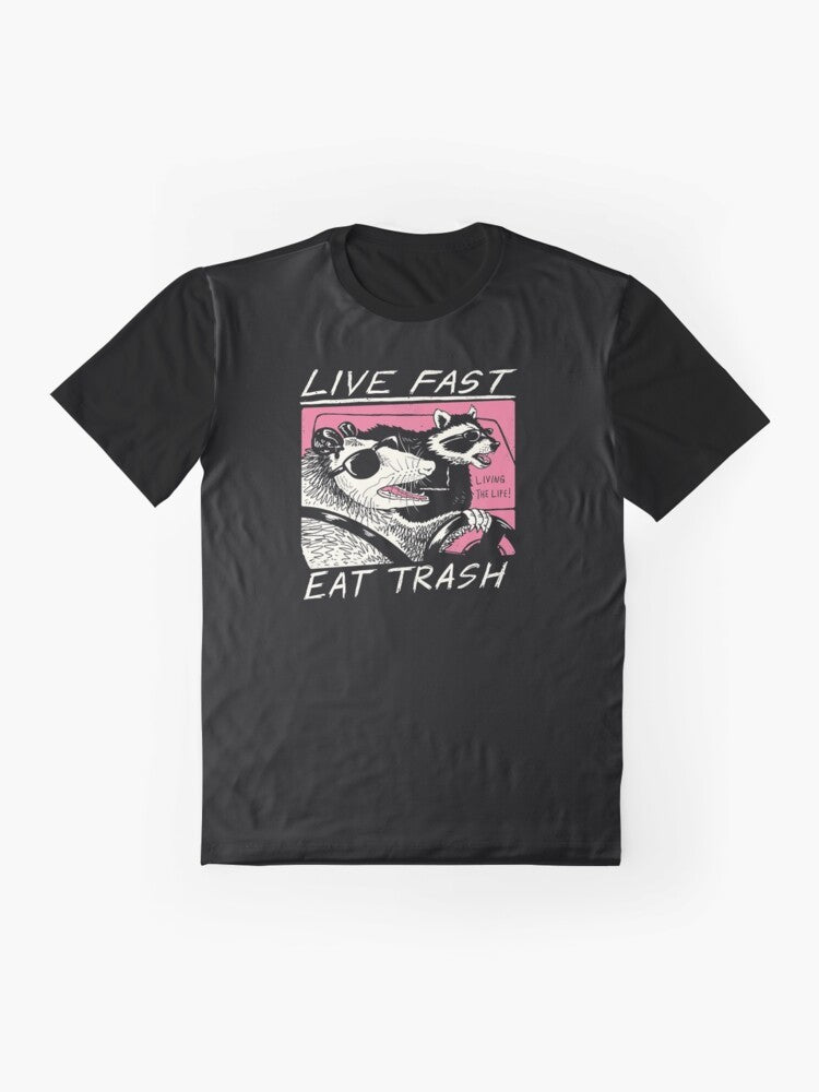 A graphic t-shirt with a live fast, eat trash design featuring a raccoon in a retro-style illustration. - Flat lay