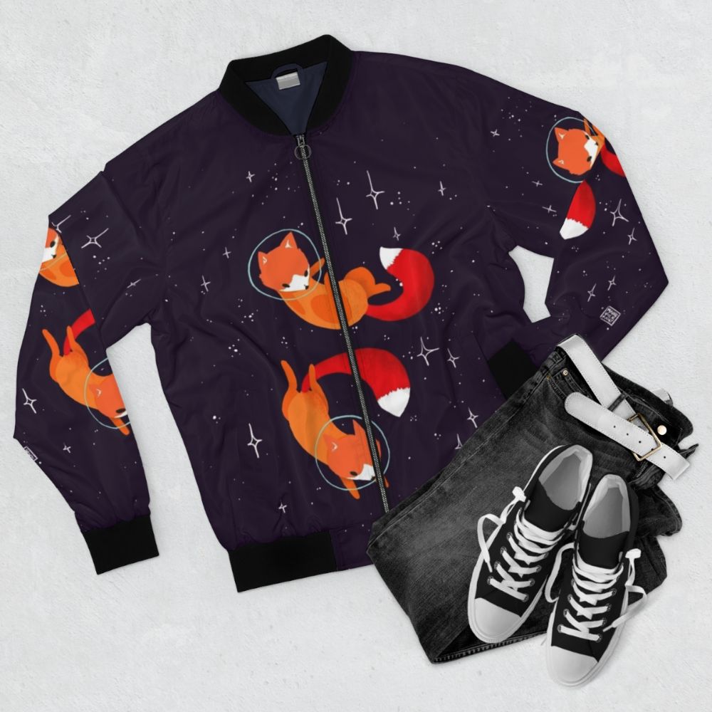 A stylish bomber jacket featuring a cute and whimsical space fox design, surrounded by stars and cosmic elements. - Flat lay