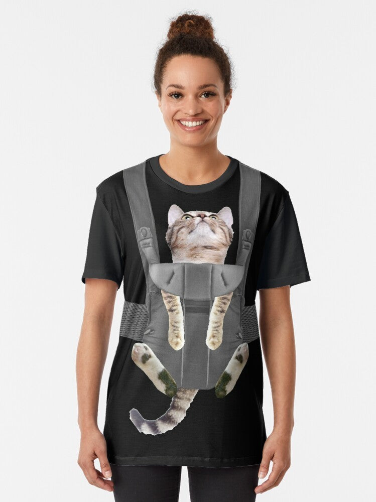 A tabby cat sitting in a baby carrier on a graphic t-shirt - Women