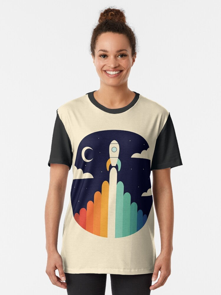 A graphic t-shirt featuring a rocket ship soaring through the sky, with a rainbow and clouds in the background, representing dreams and space exploration. - Women