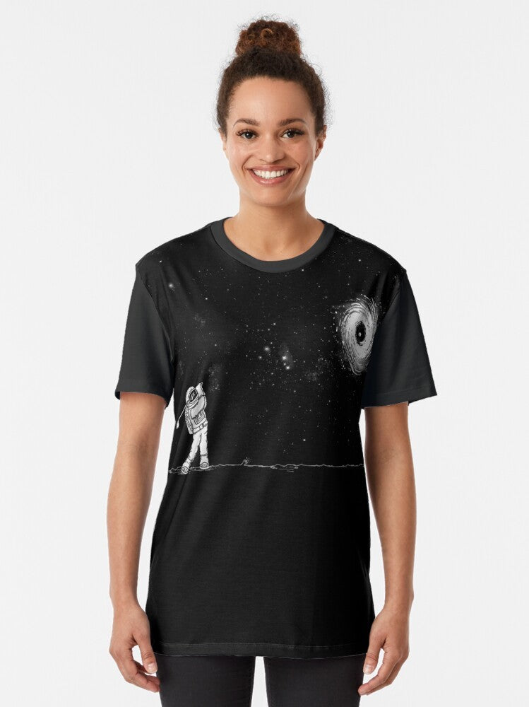 A graphic t-shirt featuring a black hole in one golf design, against a space and star-filled background. - Women