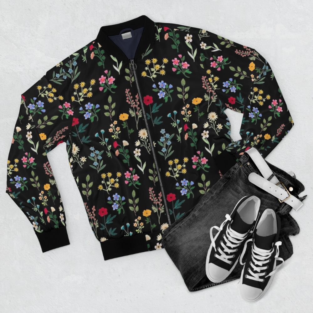 A black bomber jacket featuring a vibrant floral and botanical watercolor pattern design. - Flat lay