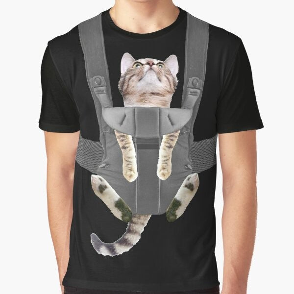 A tabby cat sitting in a baby carrier on a graphic t-shirt