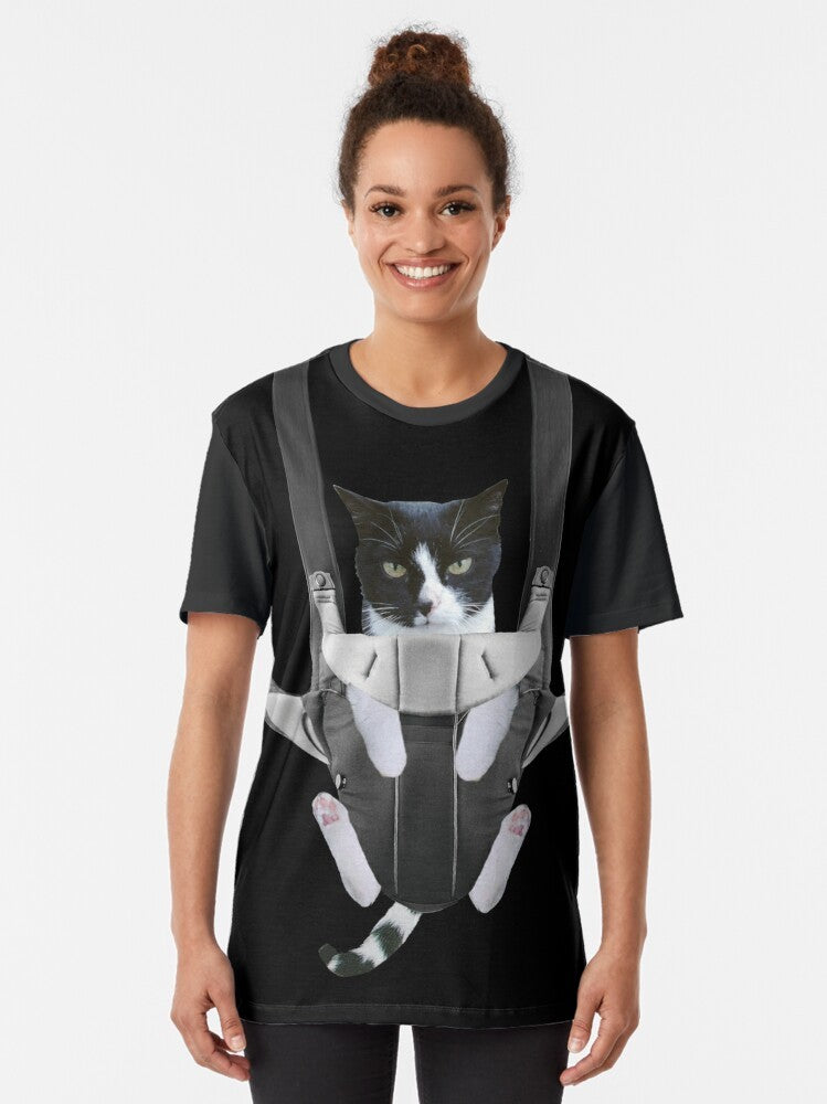 A graphic t-shirt design featuring a cute cat in a baby carrier - Women