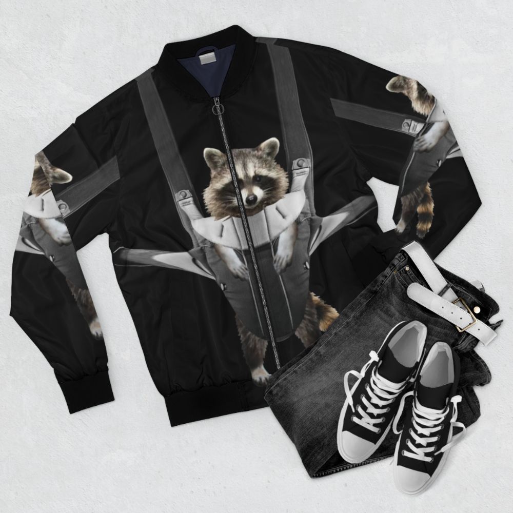 A gray and white bomber jacket with the text "Raccoon Whisperer" printed on it, featuring a playful raccoon design. - Flat lay