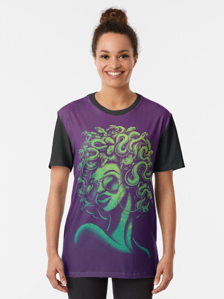 A funky and retro-inspired graphic t-shirt featuring the mythical Medusa character with an afro hairstyle and aviator sunglasses. - Women