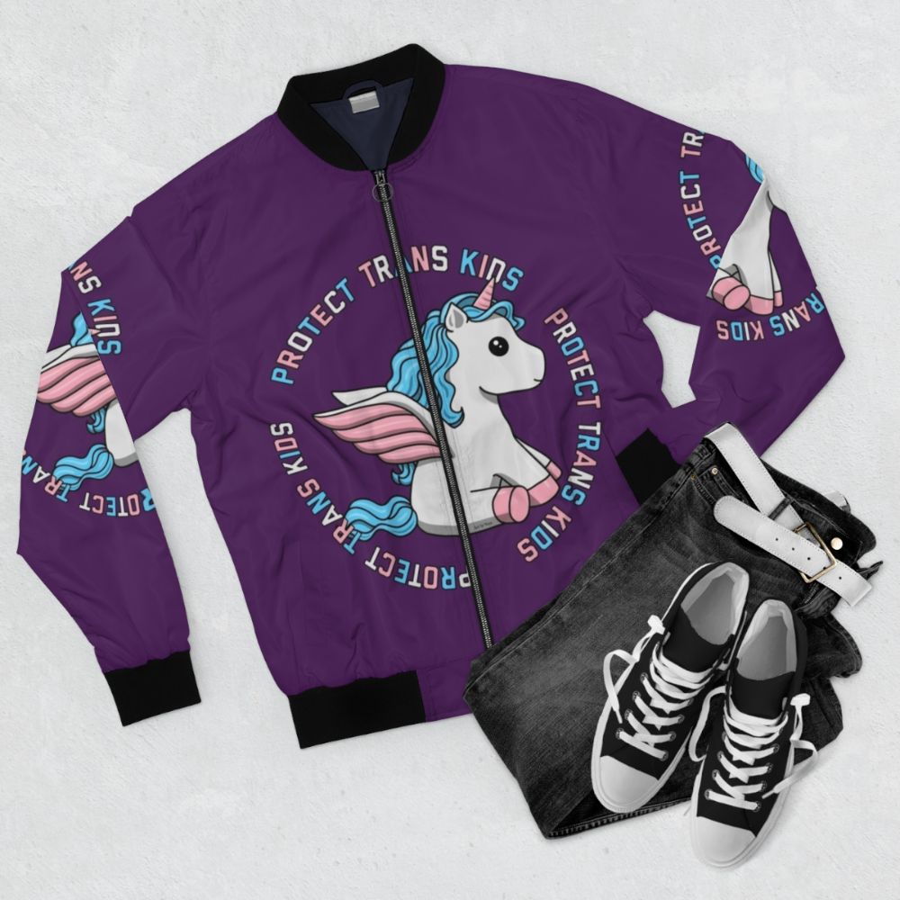 Colorful unicorn bomber jacket with trans pride colors, featuring the text "Protect Trans Kids" - Flat lay