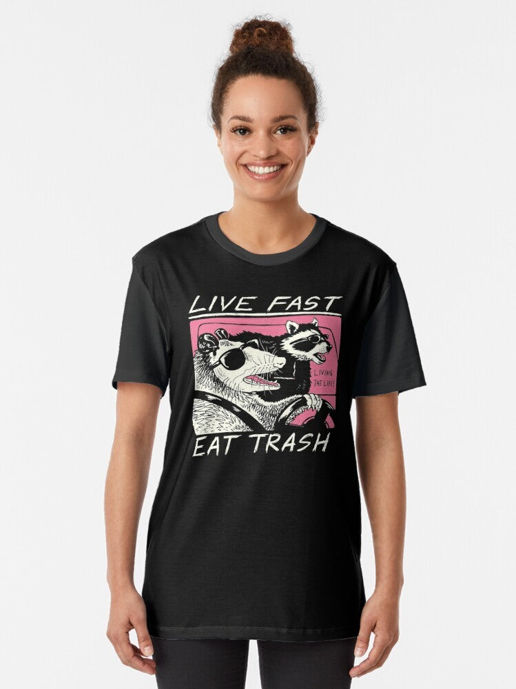 A graphic t-shirt with a live fast, eat trash design featuring a raccoon in a retro-style illustration. - Women