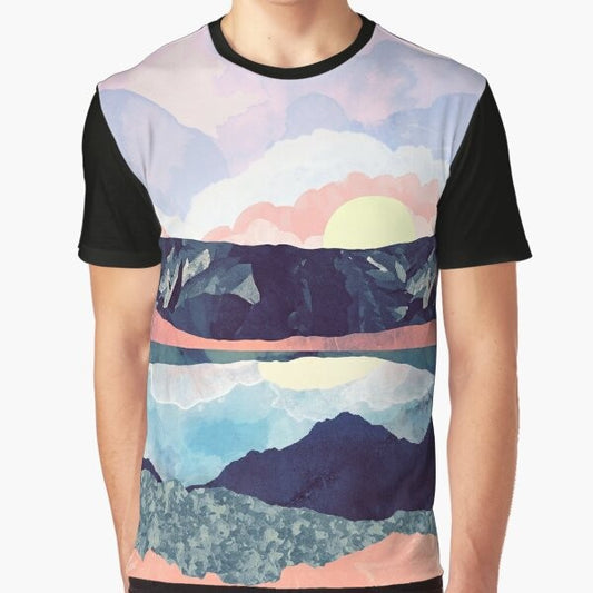 A t-shirt featuring a tranquil lake reflection with mountains, hills, and a colorful sky in shades of blue, pink, and purple.