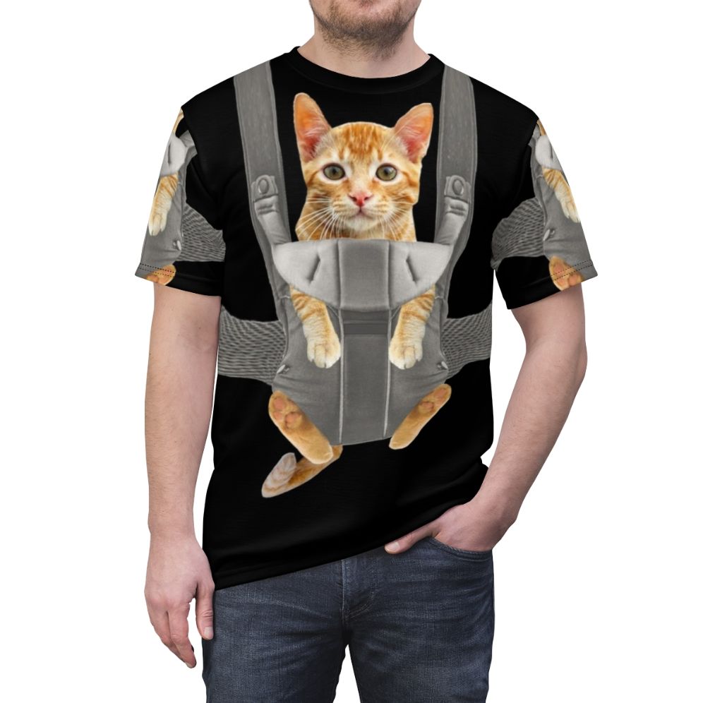 An adorable orange tabby cat named Monty sitting comfortably in a baby carrier on a t-shirt. - men front