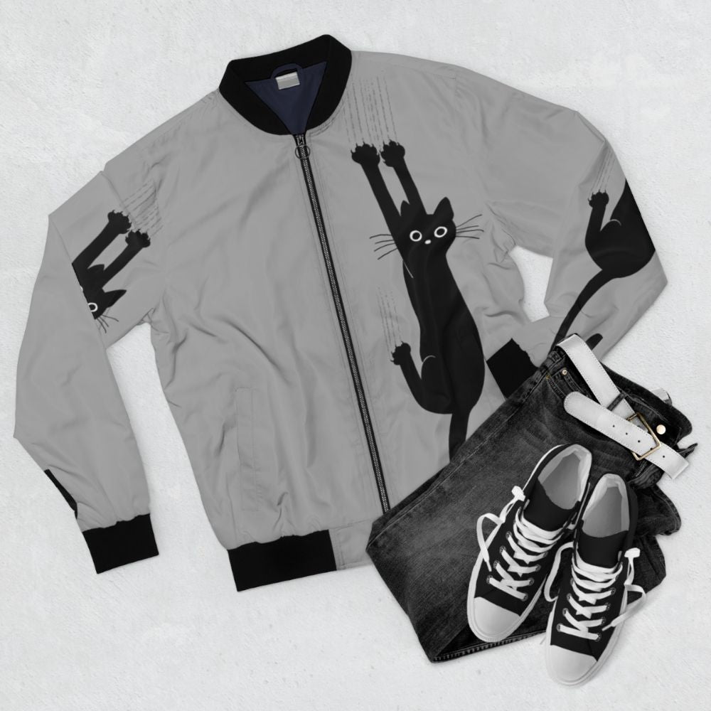 Black cat holding on to a bomber jacket with a playful, humorous expression - Flat lay