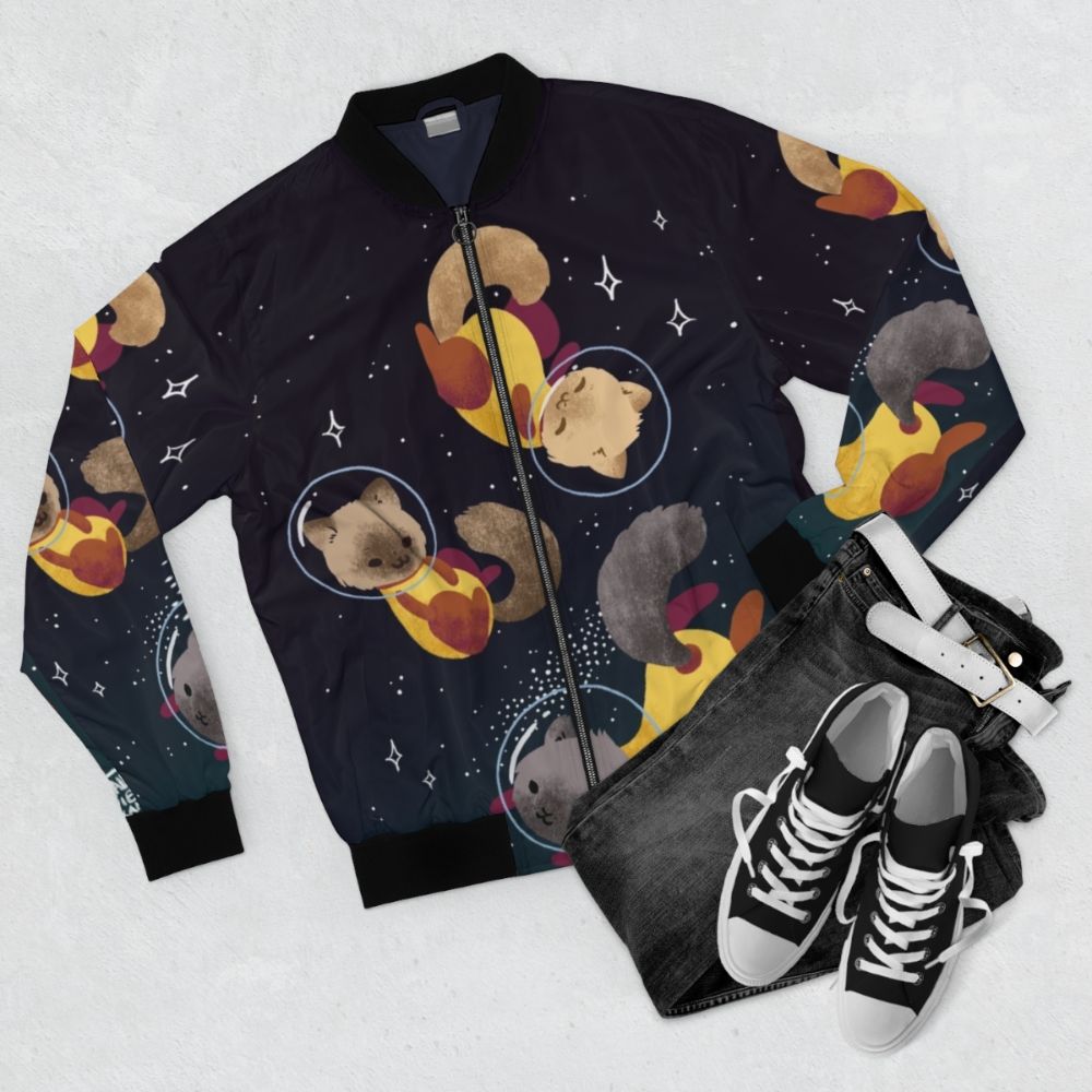 Cute and fun space cats illustration on a bomber jacket, featuring a cosmic design with stars, planets, and a playful feline astronaut. - Flat lay