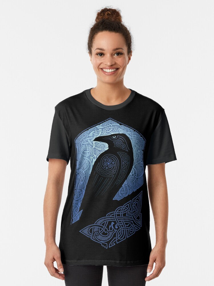 A graphic t-shirt featuring a silhouette of a raven or crow against a blue and black background with celtic and tribal design elements. - Women